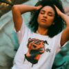 Striking portrait of a woman with curly hair and a graphic t-shirt in vibrant urban setting.