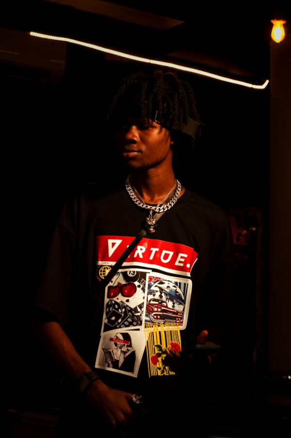 Stylish young man in graphic tee, illuminated against a dark background.